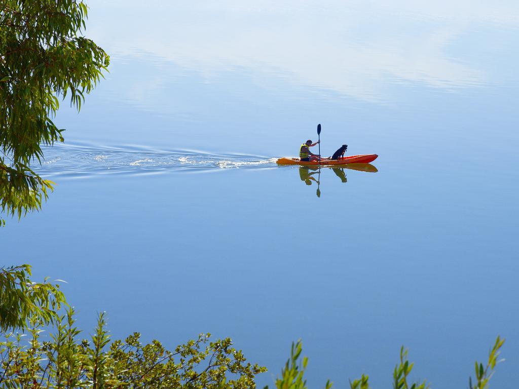 Ap Lago Montargil - Conference & Spa Екстер'єр фото The photo shows a serene scene of a person kayaking on a calm body of water. The surface of the water is very smooth, reflecting the surroundings, and there is a gentle wake behind the kayak indicating movement. The kayaker is wearing a life jacket a
