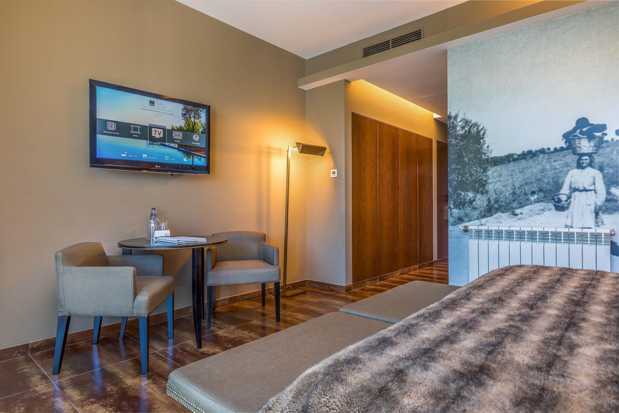 Ap Lago Montargil - Conference & Spa Екстер'єр фото The photo shows an interior of a room, likely a hotel or a modern living space. In the foreground, there is a bed with a textured brown blanket. To one side, there are two comfortable chairs and a small table, possibly with a bottle of water. A flat-