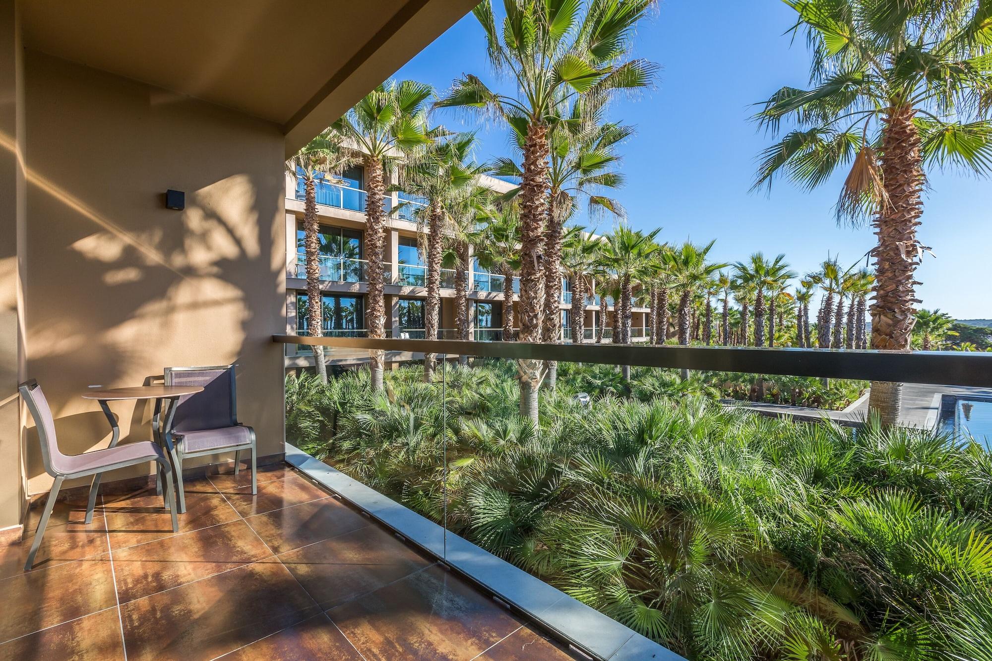 Ap Lago Montargil - Conference & Spa Екстер'єр фото The photo shows a balcony with modern furniture, including a chair and a small table. In the background, there are tall palm trees and lush greenery, suggesting a tropical or resort-like setting. The buildings in the distance are likely part of a hot