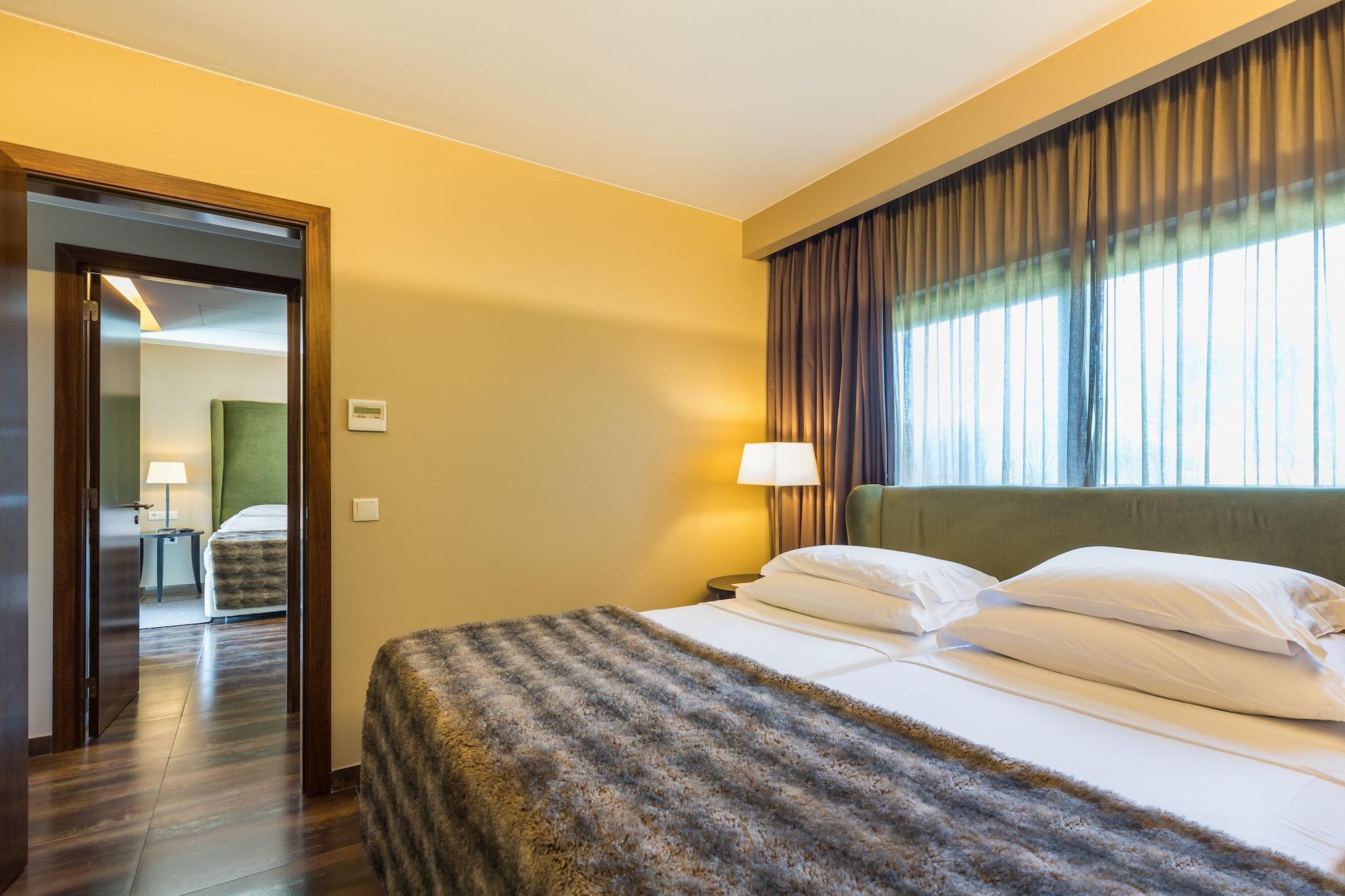 Ap Lago Montargil - Conference & Spa Екстер'єр фото The photo shows the interior of a well-furnished hotel room. It features two beds with white linens and a gray decorative throw on top. The walls are painted a warm yellow, and there are floor-to-ceiling windows covered with dark curtains that allow 