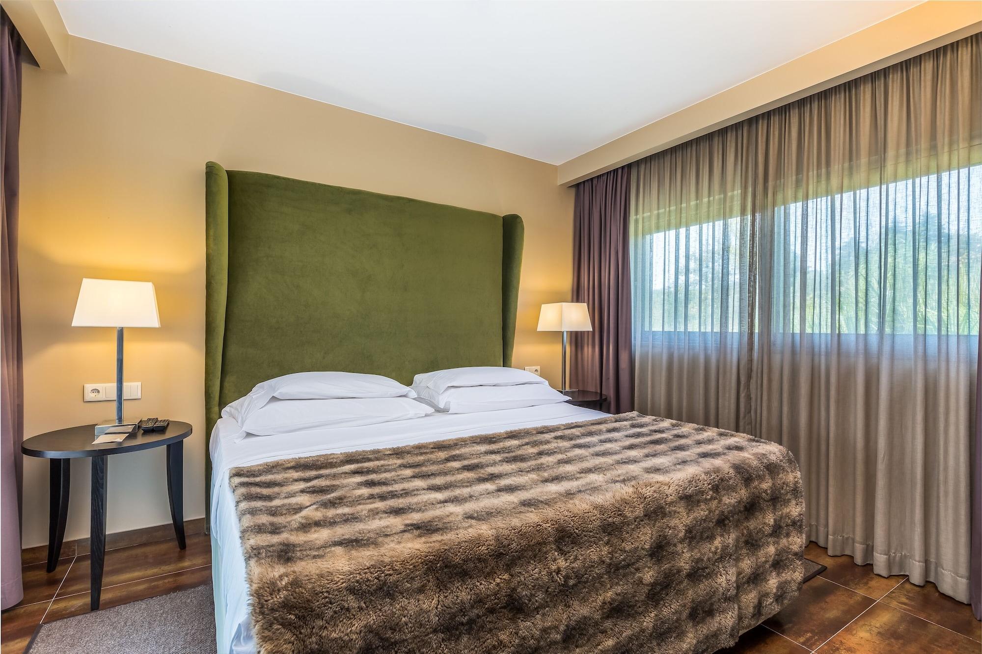 Ap Lago Montargil - Conference & Spa Екстер'єр фото The photo shows a cozy hotel room featuring a large bed with two white pillows and a fur-style blanket draped over it. Behind the bed is a tall, green headboard that adds a touch of color to the room. On either side of the bed are bedside tables, eac