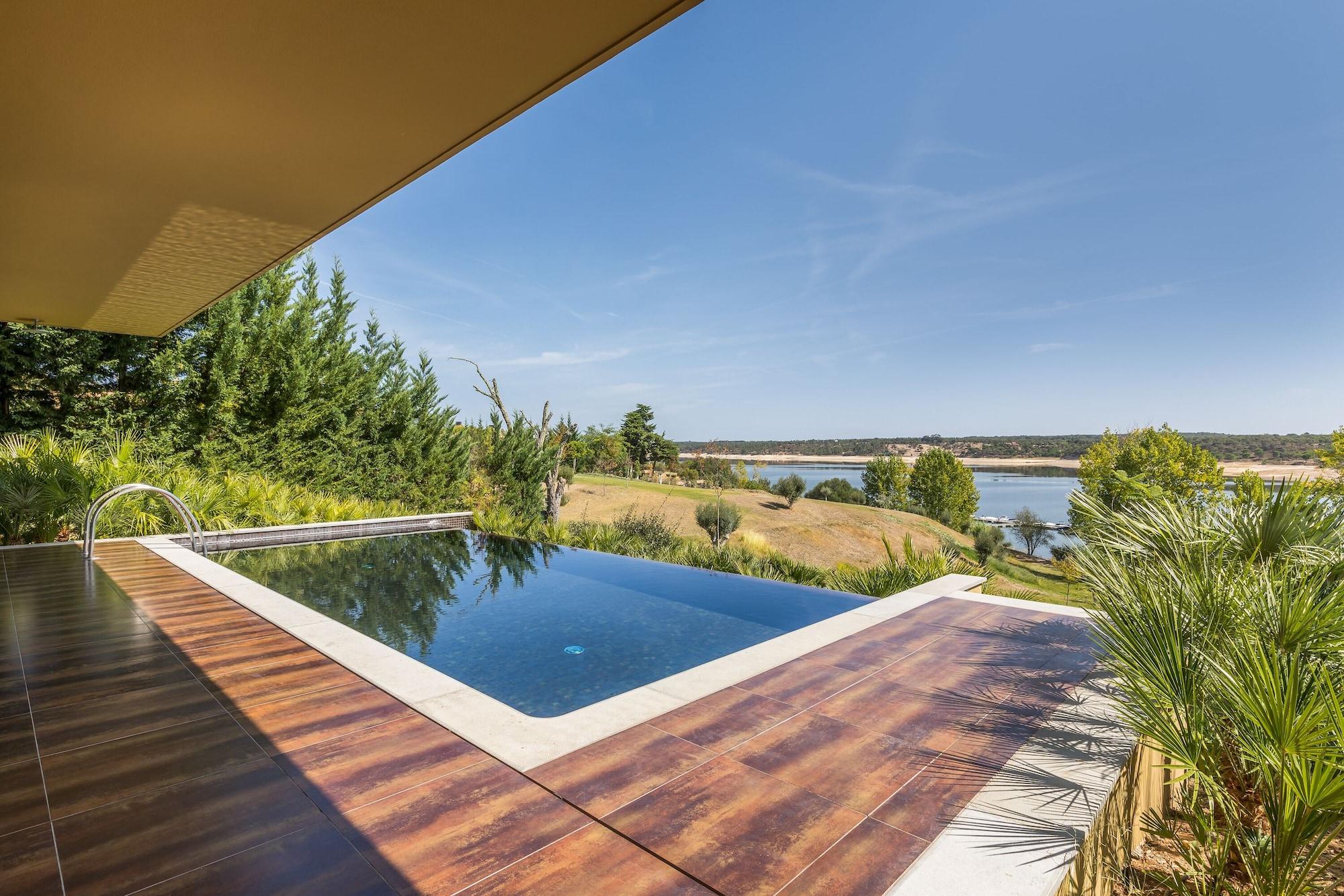 Ap Lago Montargil - Conference & Spa Екстер'єр фото The photo shows a luxurious infinity pool situated on a terrace or deck. The pool features a sleek, modern design with a dark blue surface that reflects the surrounding scenery. In the background, there is a landscape of rolling hills and a body of w