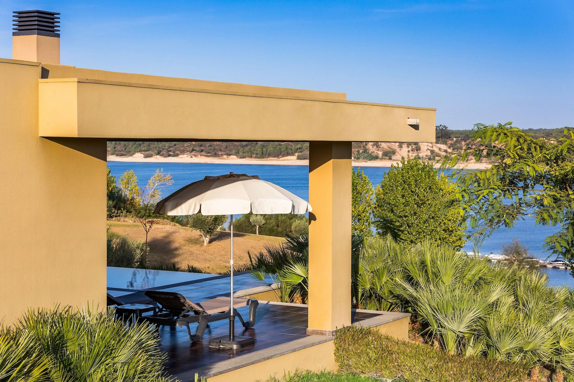 Ap Lago Montargil - Conference & Spa Екстер'єр фото The photo shows a peaceful outdoor area with a modern architectural structure featuring an overhang. There is a lounge chair positioned beneath a large umbrella, creating a shaded spot to relax. In the background, there is a picturesque view of a bod