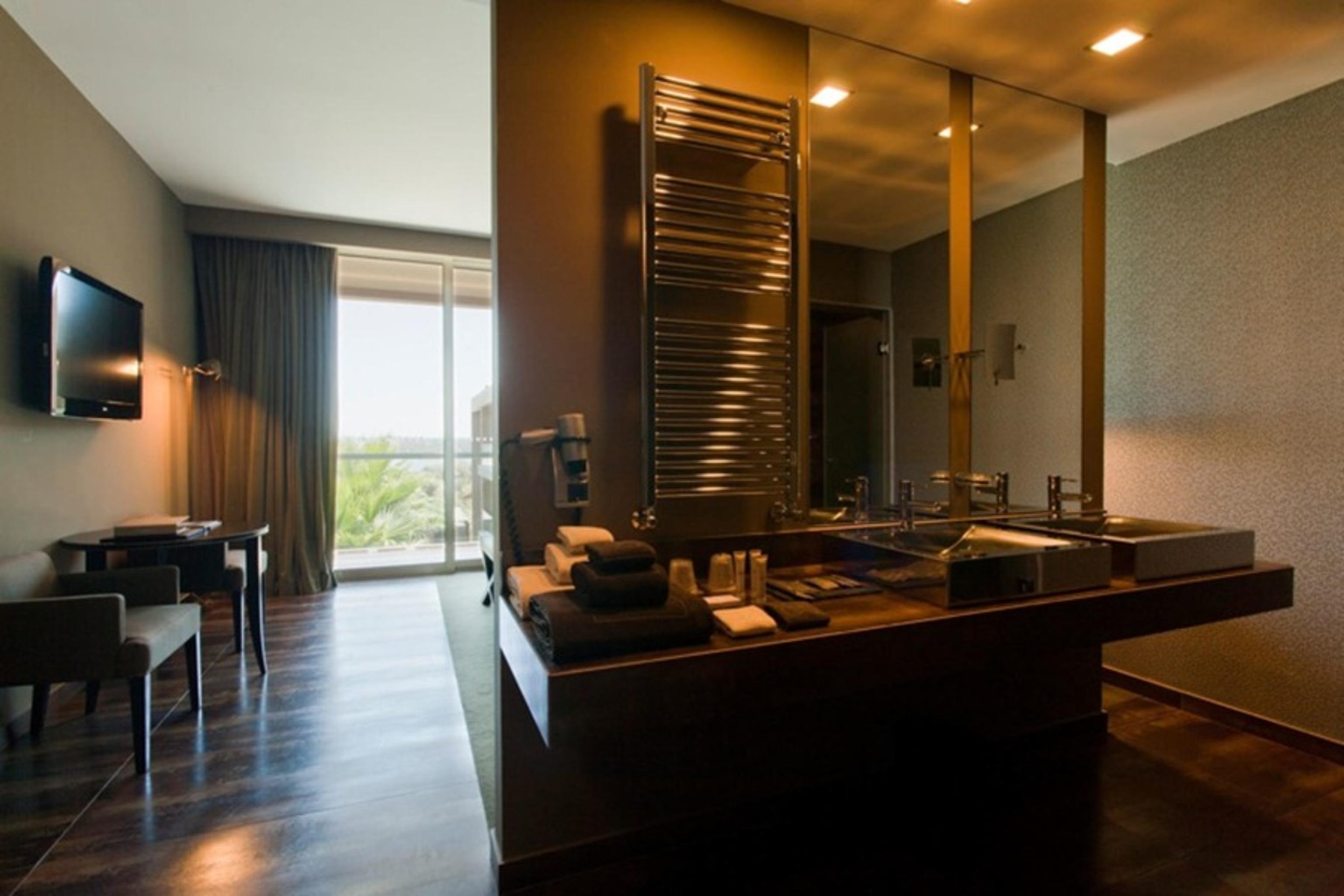 Ap Lago Montargil - Conference & Spa Екстер'єр фото The photo displays a modern hotel room with a contemporary design. The room features a large window, allowing natural light to enter and offering a view outside. On one side, there is a sitting area with a small table and chairs. The other side showc