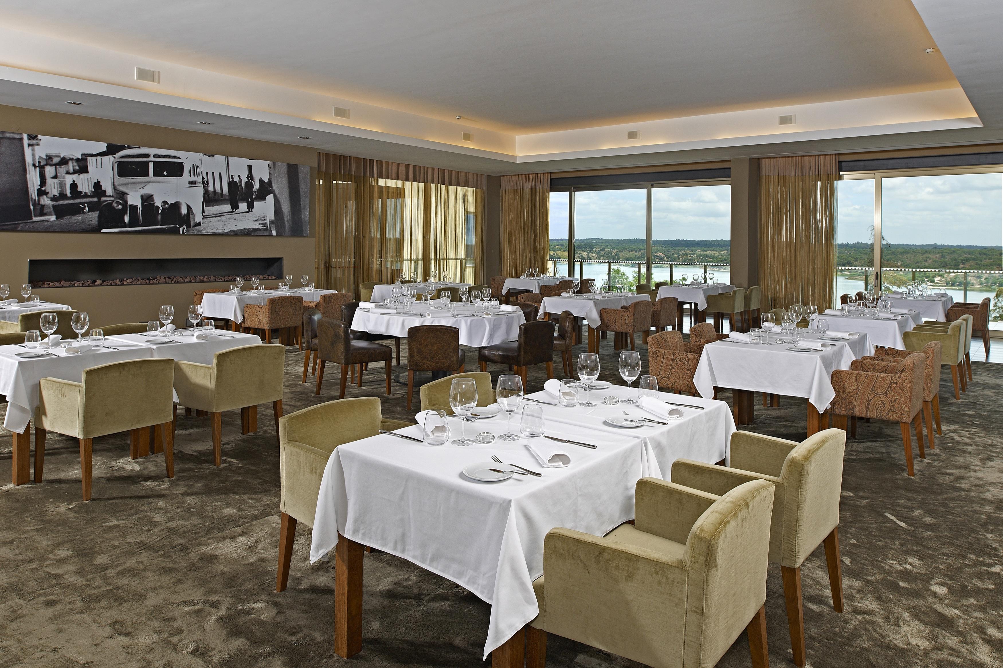 Ap Lago Montargil - Conference & Spa Екстер'єр фото The photo shows an elegant restaurant interior featuring neatly arranged tables with white tablecloths. Each table is set with plates, cutlery, and glasses. The seating includes a mix of upholstered chairs in different colors—some light and others da