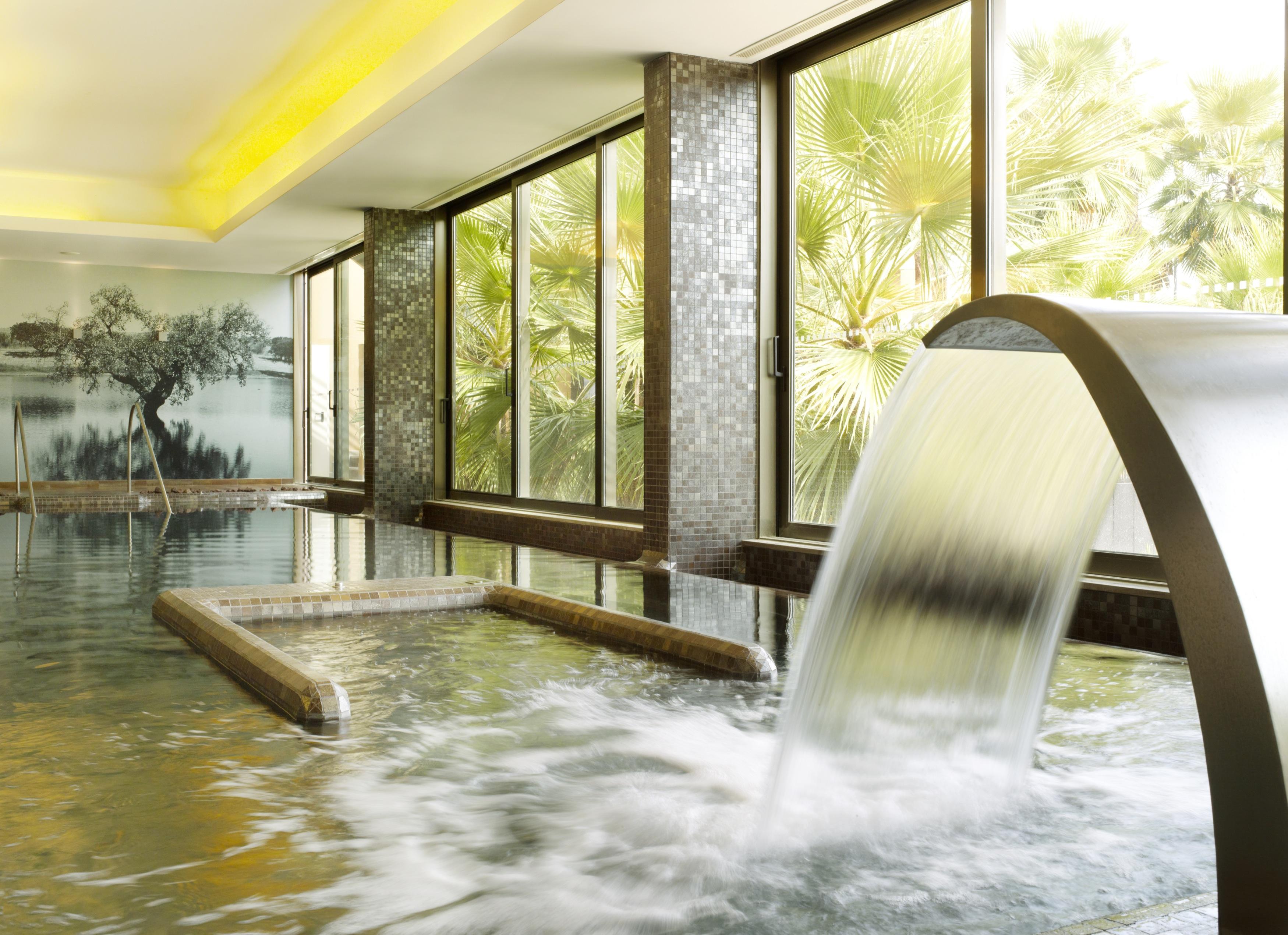 Ap Lago Montargil - Conference & Spa Екстер'єр фото The photo depicts a serene spa environment featuring a tranquil indoor pool area. There is a sleek, modern water feature that spills water gracefully into the pool. Large windows allow natural light to flood the space, showcasing views of lush greene
