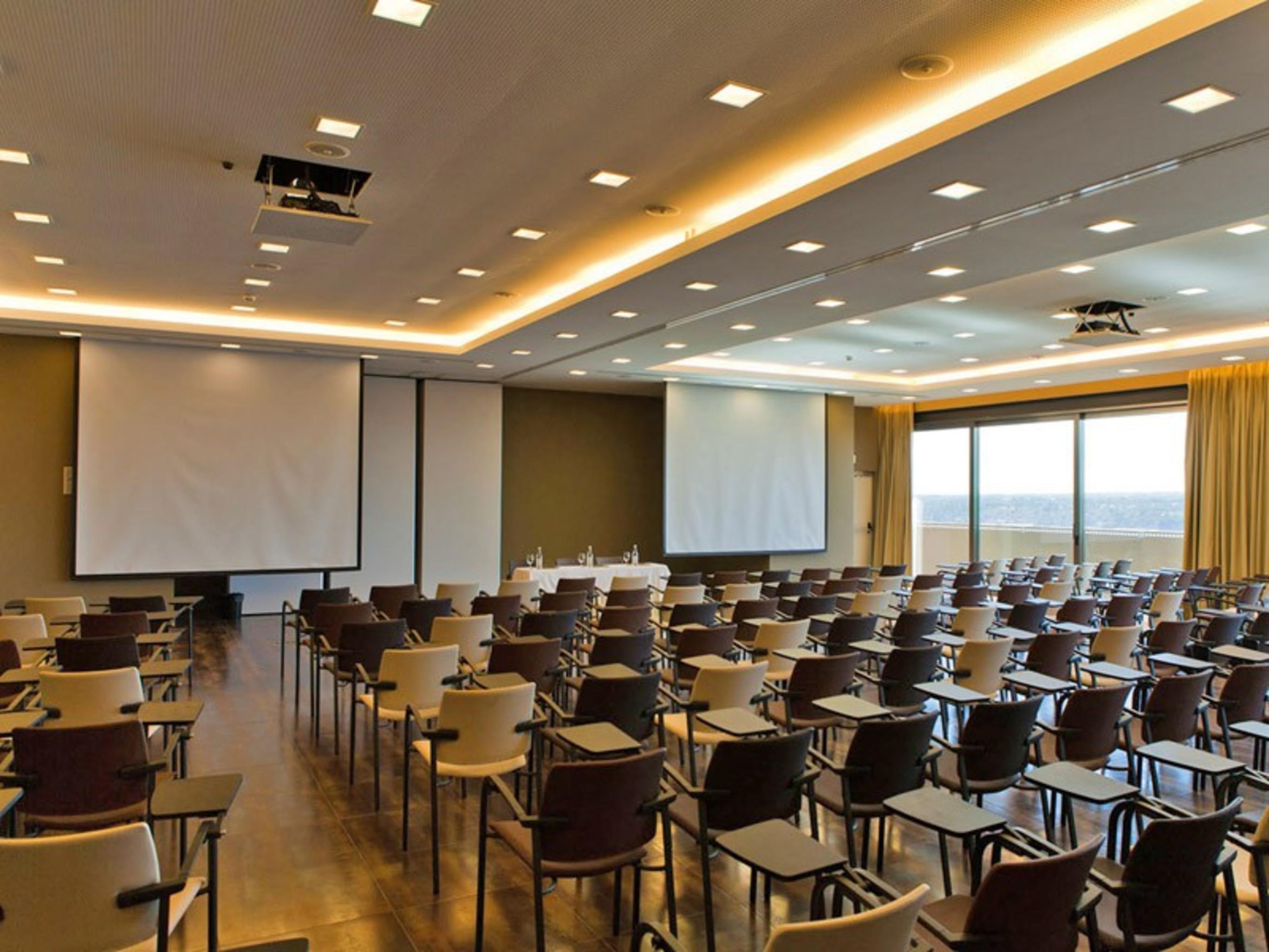 Ap Lago Montargil - Conference & Spa Екстер'єр фото The photo shows a large conference room set up for a presentation or meeting. There are multiple rows of chairs arranged in a semi-theater style, facing two large projection screens. The room has a modern design, with soft lighting and large windows 