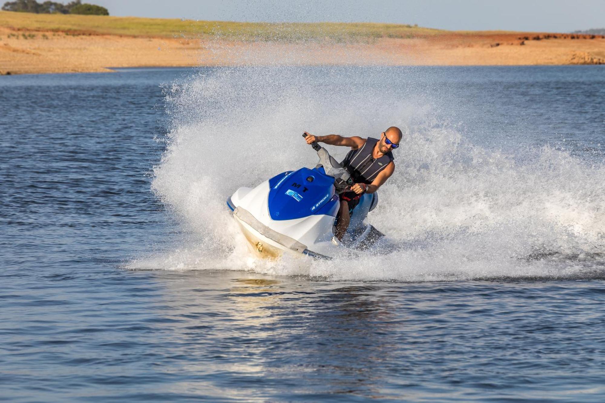 Ap Lago Montargil - Conference & Spa Екстер'єр фото The photo shows a person riding a jet ski over a body of water. The rider is wearing sunglasses and a life vest, leaning forward as the jet ski accelerates, creating a spray of water around them. The background features a natural landscape, likely a 