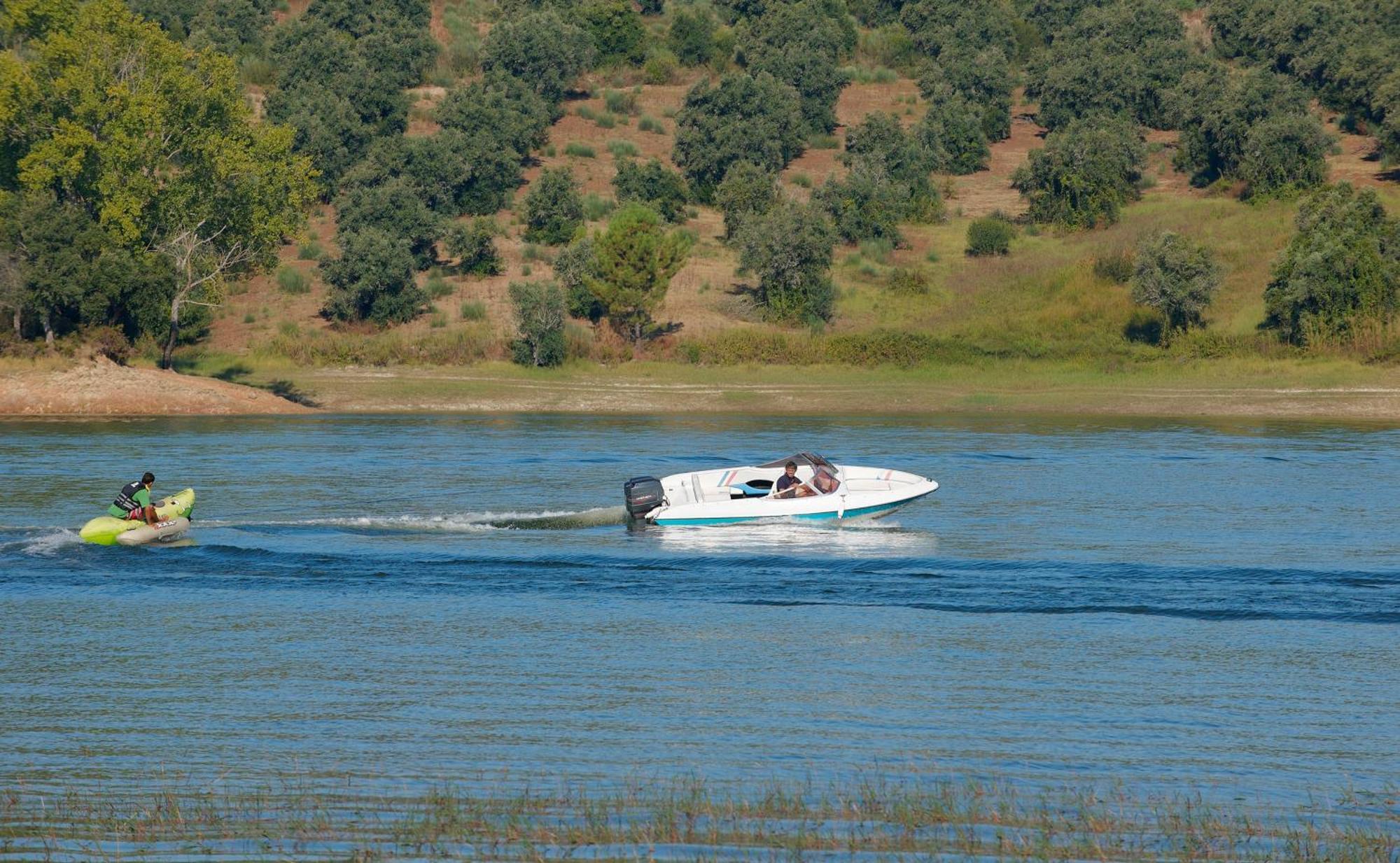 Ap Lago Montargil - Conference & Spa Екстер'єр фото The photo shows a scene on a water body, likely a river or lake. In the foreground, a speedboat is moving quickly through the water, leaving a wake behind it. There are two people visible in the boat. In the background, there is a hilly area covered 